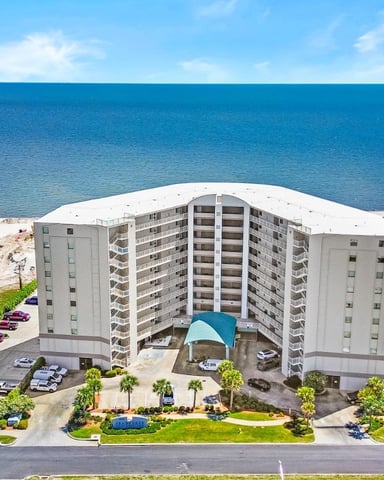 Beachfront condominium building with white facade overlooking turquoise water and sandy beach