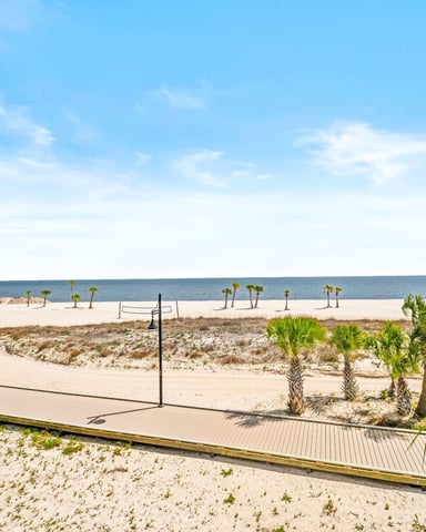 Beach with sandy dunes, palm trees, volleyball net, and calm gulf waters under clear blue sky