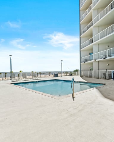 Beachfront high-rise resort pool deck with lounge chairs, ocean view, and blue sky