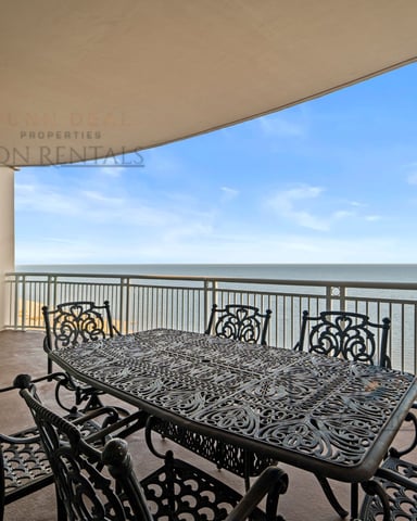 Beachfront balcony with ornate black dining table, chairs, and ocean view under clear blue sky