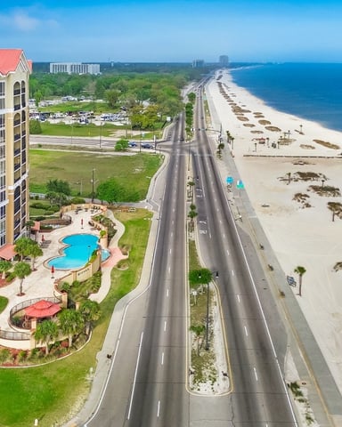Beachfront condo tower with red roof and pool overlooking sandy beach and ocean highway