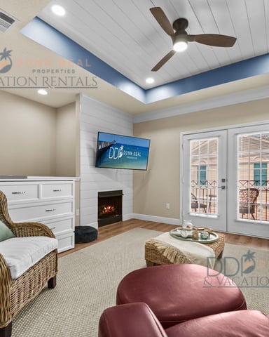 Modern living room with coffered ceiling, ceiling fan, fireplace, wicker chair, cream sofa, and glass doors opening to balcony