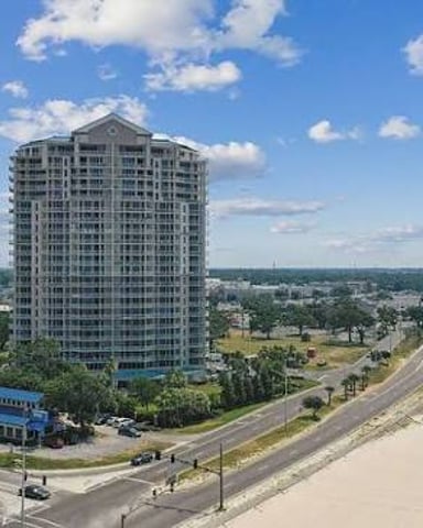 Tall residential tower overlooking beach, sand dunes, and coastal highway with green landscape beyond