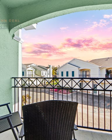 Balcony with black railing and lounge chairs overlooking residential street at sunset