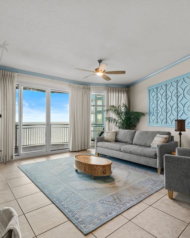 Bright living room with gray sofas, tile flooring, blue-trimmed ceiling, and ocean view from balcony doors
