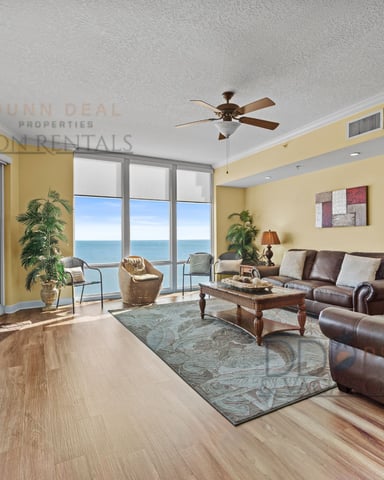 Spacious living room with yellow walls, brown leather furniture, ocean view through floor-to-ceiling windows, and ceiling fan