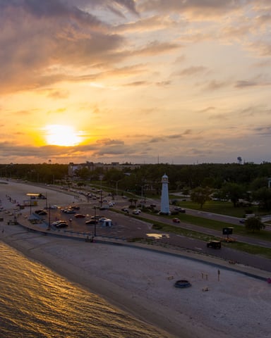 Sunset over beach with lighthouse, boardwalk, and waterfront homes along sandy shore