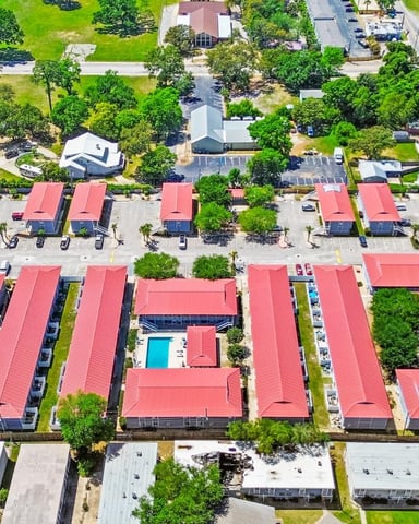Aerial view of residential neighborhood with red-roofed townhouses, swimming pools, parking areas, and mature trees