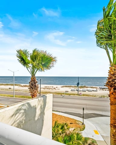 Beachfront property with palm trees, ocean view, boardwalk, and sandy beach under clear blue sky