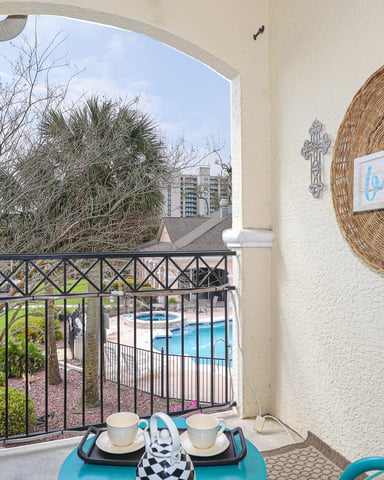 Balcony with wicker beach sign, turquoise table, and view of pool and palm trees