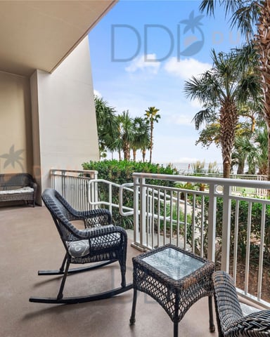 Covered balcony with wicker furniture and white railing overlooking palm trees and coastal landscape