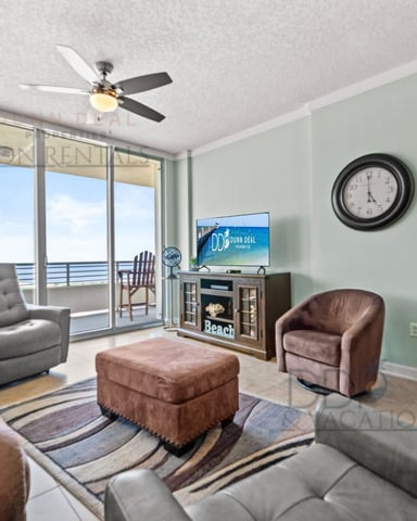 Beachfront condo living room with ocean view balcony, ceiling fan, TV, upholstered seating, and mint green walls