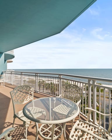 Oceanfront balcony with metal furniture, white railing, and clear view of calm sea and sky