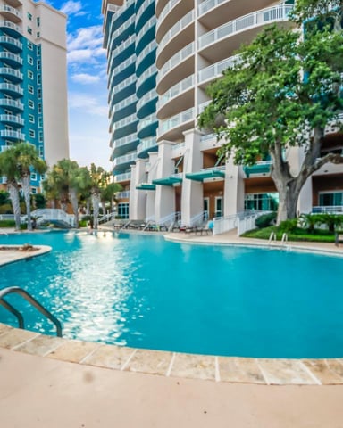 Resort pool with curved edges surrounded by high-rise condominiums, palm trees, and lounge chairs