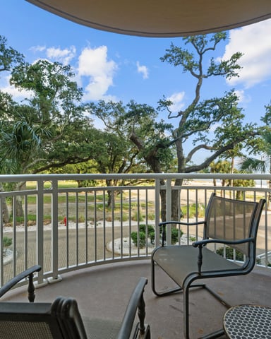 Curved balcony with metal railing and lounge chairs overlooking mature oak and palm trees with manicured grounds