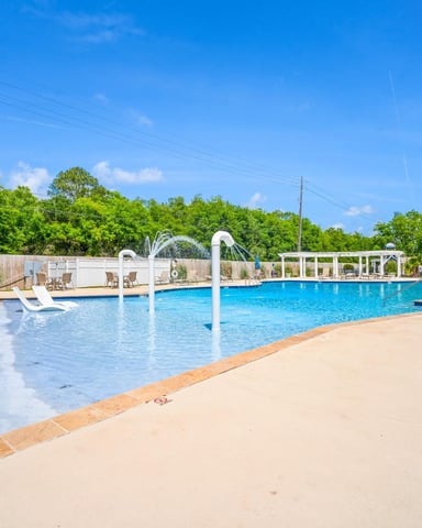 Large community swimming pool with diving board, white pergola, lounge chairs, and water tower under clear blue sky