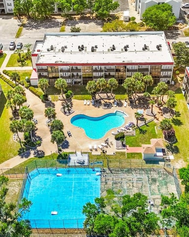 Aerial view of apartment complex with two pools, surrounding buildings with red trim, and landscaped courtyards