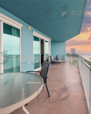 High-rise beachfront balcony with dining table, lounge chairs, and sunset ocean view