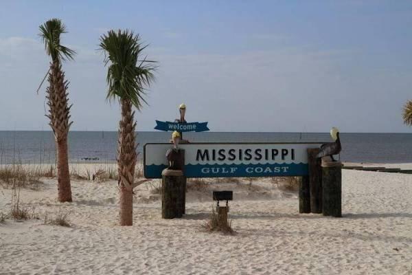 Welcome to Mississippi Gulf Coast sign on sandy beach with palm trees and ocean view