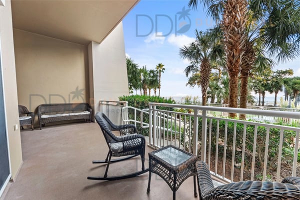 Covered balcony with wicker furniture overlooking palm trees and coastal landscape under clear blue sky